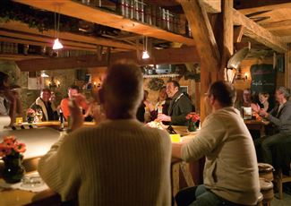 A cozy bar with wooden furniture and warm lighting. People are sitting at the counter and having a good time together.