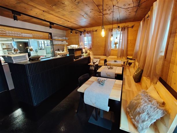 A cozy restaurant with wooden interiors and warm lighting. The tables are neatly set and offer an inviting atmosphere.