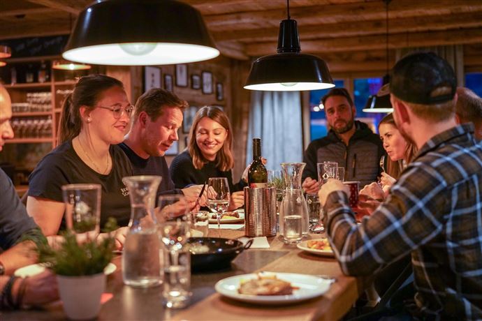 A group of people is sitting at a table and enjoying a shared meal. There is a pleasant atmosphere with warm lighting.