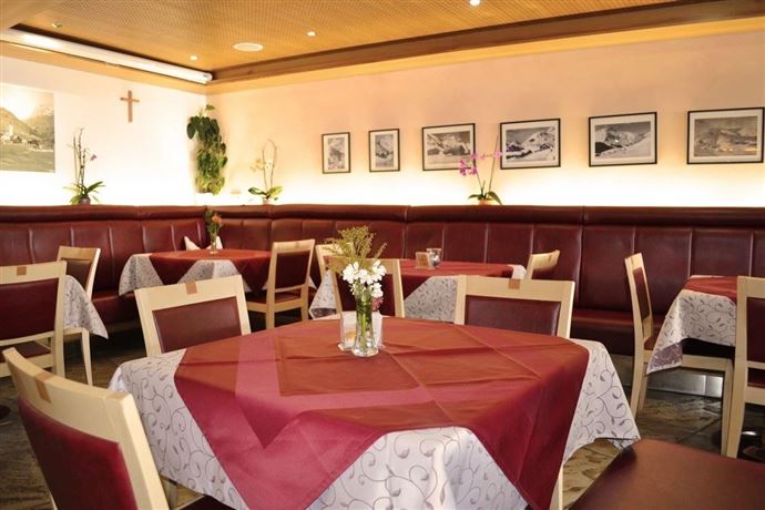 A cozy restaurant with red benches and tables. Pictures hang on the walls, and flower vases are on the tables.