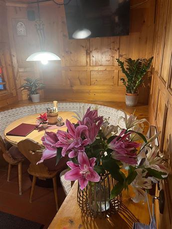 A cozy dining area with wood paneling and a round table. On the table is a vase with colorful lilies, and there are some plants in the background.