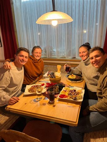 A group of four people is sitting at a table and enjoying a meal together. Various dishes and drinks can be seen on the table.