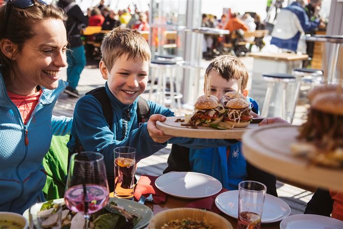 A cheerful family sits together and enjoys delicious snacks and drinks. The children are delighted with the tasty burgers that are being served.