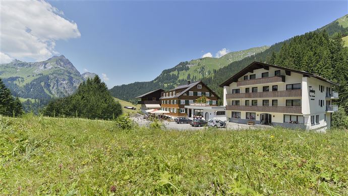 A picturesque hotel in a mountainous landscape. Surrounded by green meadows and majestic mountains under a clear blue sky.