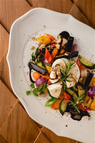 A colorful vegetable dish on a white plate. The fresh ingredients are beautifully arranged and garnished with herbs.