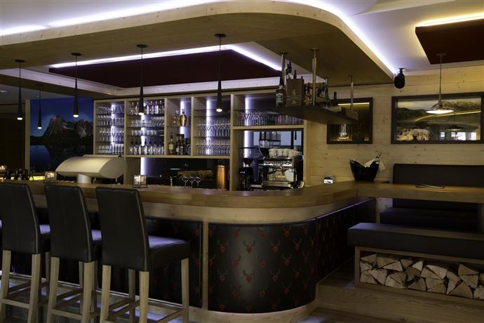 A modern bar with wooden interiors and elegant lighting. The space is well-equipped with seating and a glass display case.