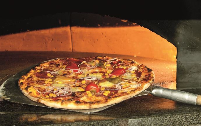 A freshly baked pizza with tomatoes, onions, and cucumbers is taken out of the oven. The oven in the background displays a warm, inviting atmosphere.