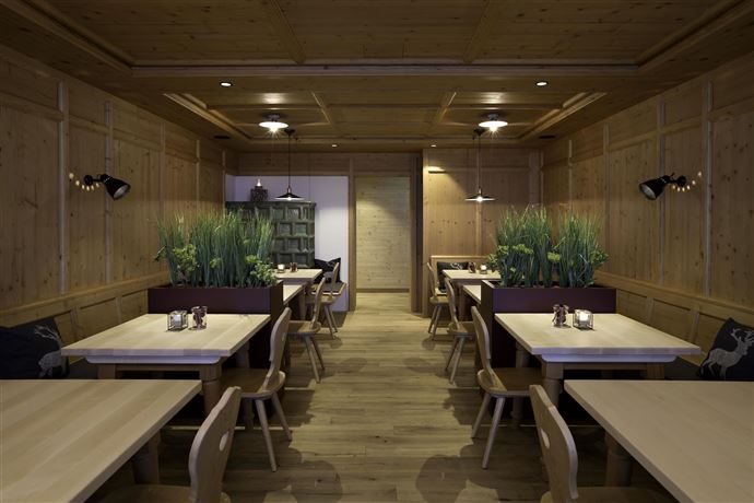 A cozy restaurant with wood paneling and plants. There are several tables that invite you to linger.