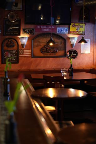 A cozy bar with a wooden counter and many wall decorations. On the table, there is a vase with a plant and a bottle of wine.