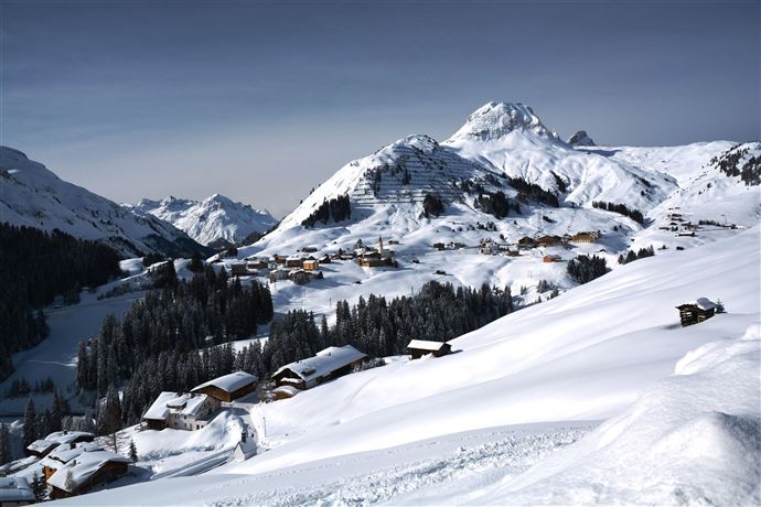 Een besneeuwd berglandschap met traditionele hutten. De majestueuze bergen rijzen omhoog onder een heldere lucht.