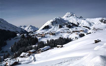 Eine verschneite Berglandschaft mit traditionellen Hütten. Die majestätischen Berge erheben sich unter einem klaren Himmel.