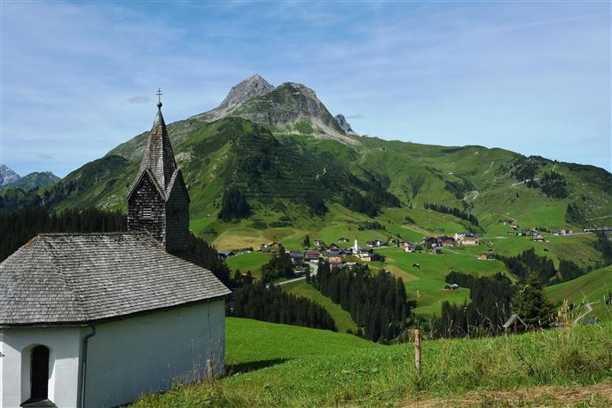 A scenic landscape with gentle hills and a mountain in the background. In the foreground stands a small church, surrounded by green meadows.