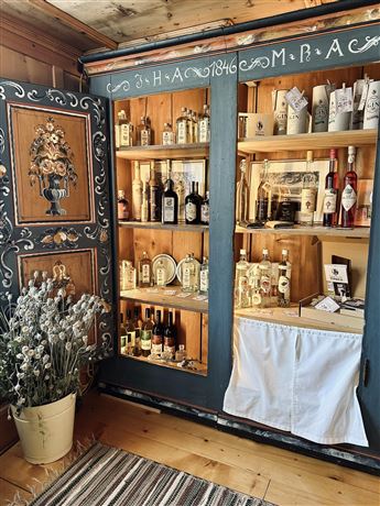 A traditional wooden cabinet with various spirits and bottles. Next to it is a pot with dried flowers on a patterned carpet.