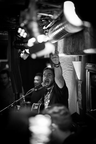 A musician is on stage playing guitar. He sings and is having fun while the audience cheers him on.