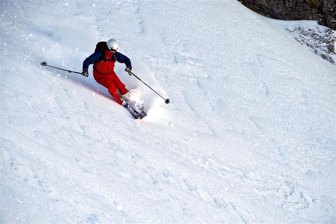 Ein Skifahrer fährt auf einer verschneiten Piste. Die Umgebung ist klar und winterlich.