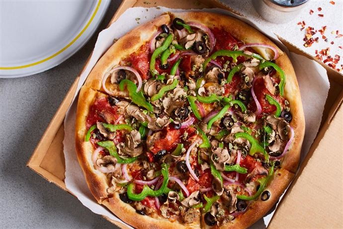 Eine köstliche Pizza mit einer Vielzahl von Belägen, darunter Paprika, Zwiebeln, Oliven und Pilze. Sie liegt in einer Pizzaschachtel auf einem Tisch.