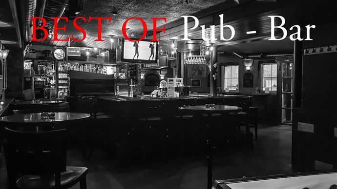 A cozy pub with dark interiors and standing tables. TVs hang on the wall and a bar is visible in the background.