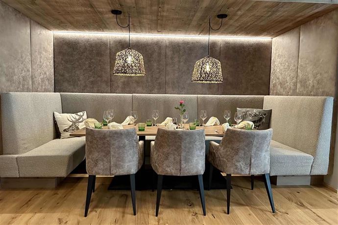 An elegant dining area with a cozy bench and stylish chairs. The tables are festively set and illuminated with beautiful lamps.