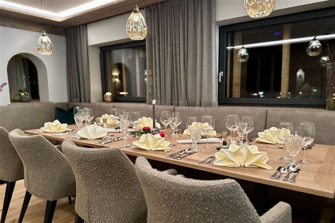 An elegant dining area with a long table, decorated with white napkins and glassware. The room is softly lit and conveys a cozy atmosphere.