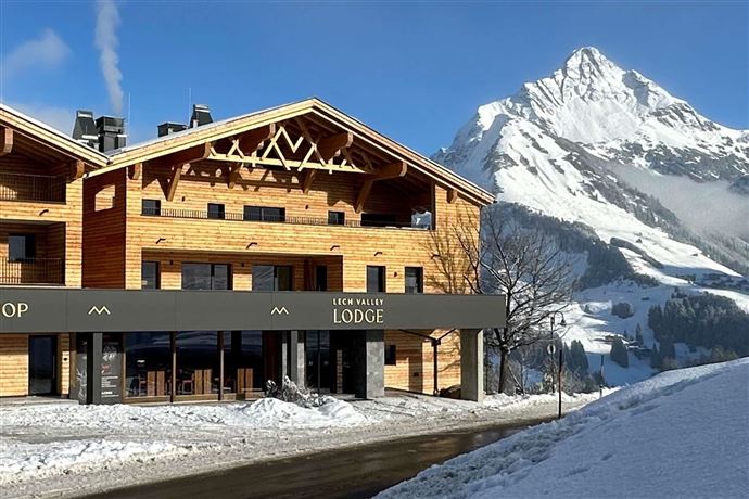 A cozy wooden lodge in a snow-covered landscape. In the background, a majestic mountain rises into the sky.