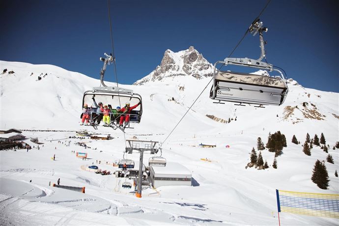 A sunny winter scene with ski lifts and snow. In the background, a mountainous panorama can be seen.