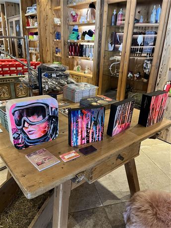 A wooden table with various artistic boxes and merchandise items. In the background, products on shelves can be seen, creating a cozy shopping environment.