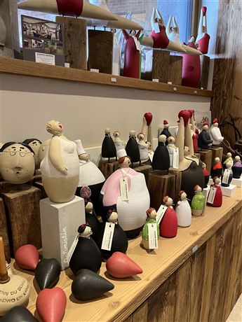 A collection of colorful clay figures stands on a wooden shelf. The figures have different shapes and colors and are creatively designed.
