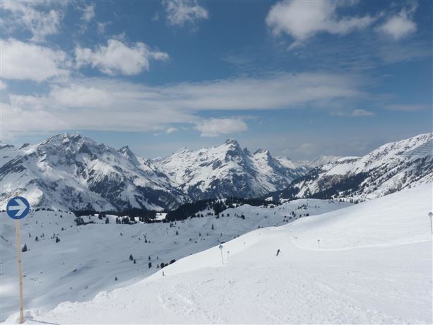 A picturesque winter landscape with snow-covered mountains and a clear sky. The sun shines on the untouched blanket of snow.