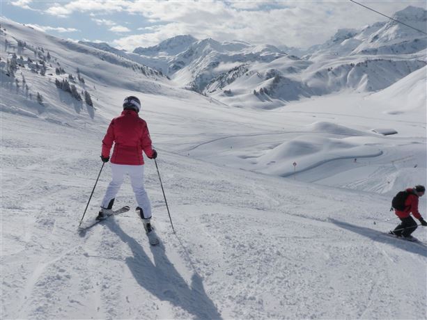 A person is skiing in the snowy mountains. The landscape is surrounded by white snow and tall mountains.