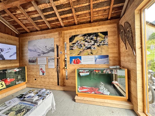 A cozy room with wooden paneling and exhibitions about winter sports. Pictures and information hang on the walls, while a display case with equipment stands prominently in the foreground.