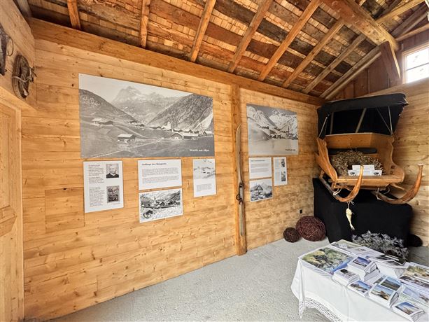 A traditional room with wooden walls and historic decor.  
Black and white pictures and informative panels about the region hang on the walls.