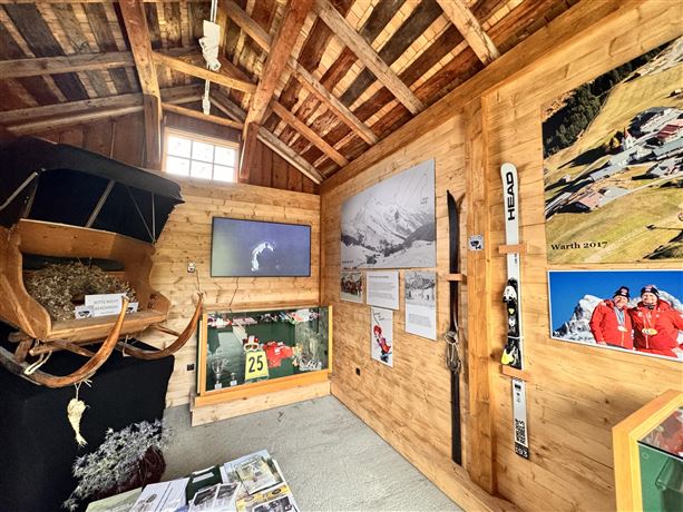 A cozy room with wooden paneling, displaying various exhibits and information about winter sports. On the wall, there are photos and ski equipment visible.