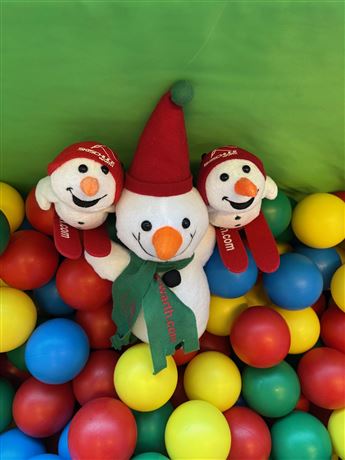 Three cheerful snowmen are standing in a colorful ball pit. The colored balls are red, blue, yellow, and green.