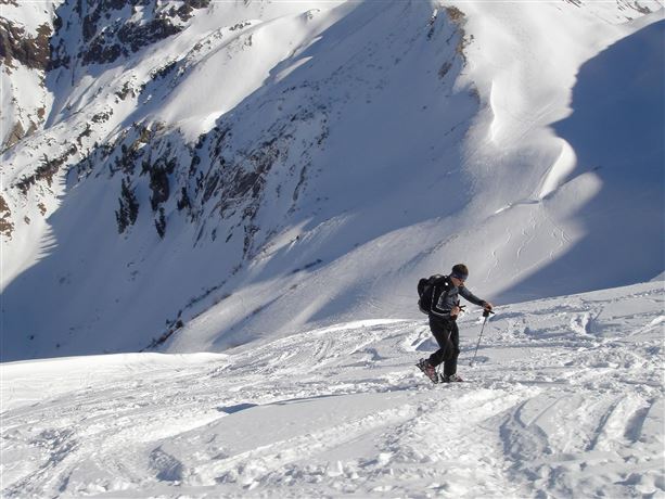 A climber hikes across a snow-covered landscape. The surroundings are surrounded by steep, snow-covered slopes.