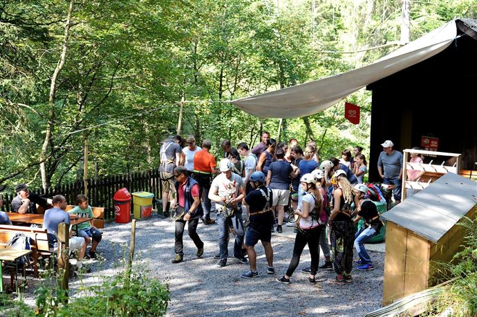 Een groep mensen verzamelt zich bij een bosstand met tafels buiten. Op de achtergrond zie je bomen en een ontspannen sfeer.