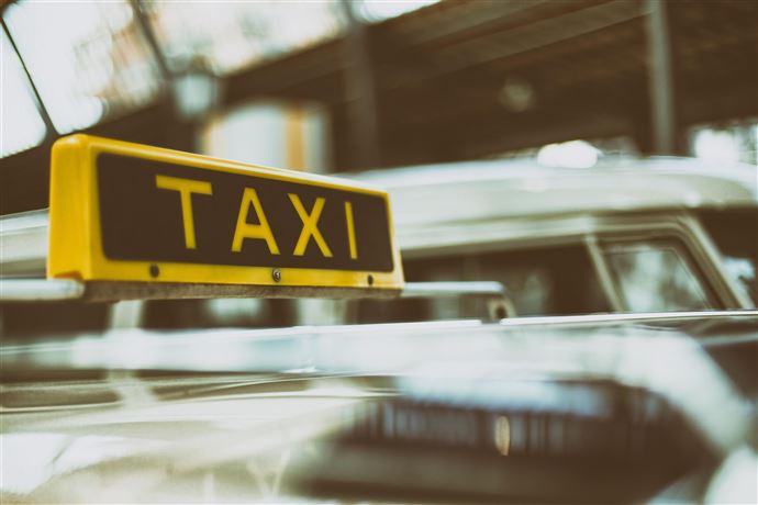 A taxi with a yellow sign on the roof. It is located in an urban environment.