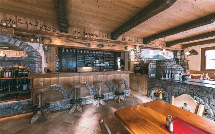 A cozy interior of a restaurant with a wooden beam and stone walls. The bar is well-equipped and the decor radiates a warm, inviting atmosphere.