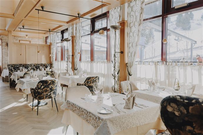 An elegant restaurant with stylish tables and floral decor. Large windows let in plenty of daylight and offer a view outside.