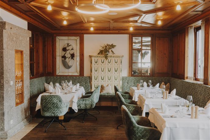 A cozy restaurant with wooden decor and green upholstered furniture. Elegant tables are set for guests.