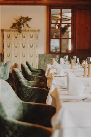 An elegant restaurant with a beautifully set table and green chairs. In the background, a window and a decorative dresser are visible.