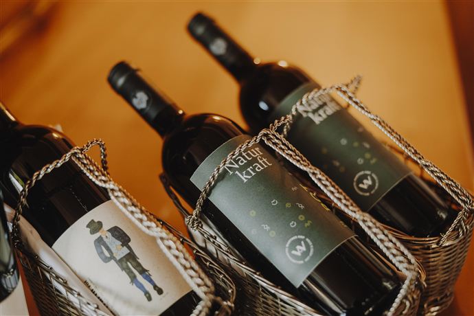 Three bottles of red wine in baskets, one of them with a labeled picture of a man. The labels feature different designs and lettering.