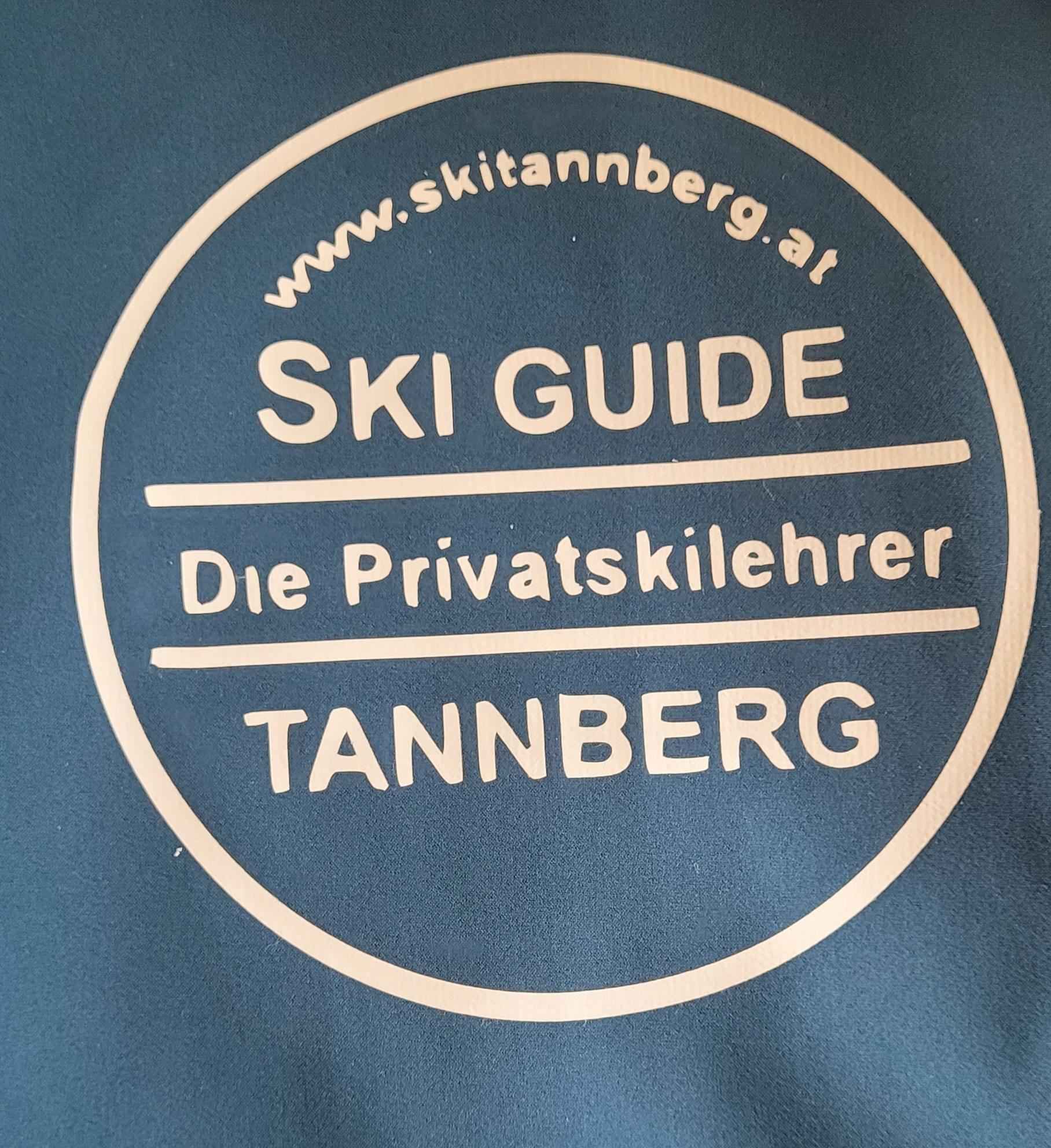 A blue fabric with a white logo for a ski guide. The text describes private ski instructors in Tannberg and includes the website.