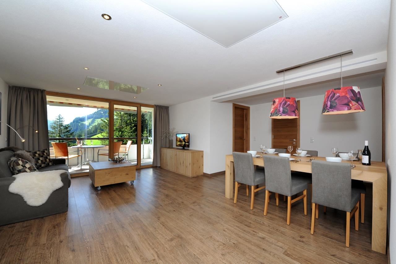 A modern living room with a cozy seating area and a dining table. Large windows offer a view of the mountains and plenty of daylight.