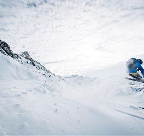 A smiling child is sitting in a yellow tire on the snow. In the background, more children and a sledding access facility can be seen.