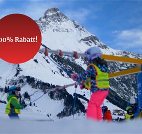 Children are skiing in the mountains. In the background, a beautiful snow-covered peak can be seen.