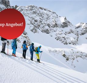 A group of skiers is standing on a snowy slope in front of impressive mountains. The text "Top Offer!" refers to a special deal.