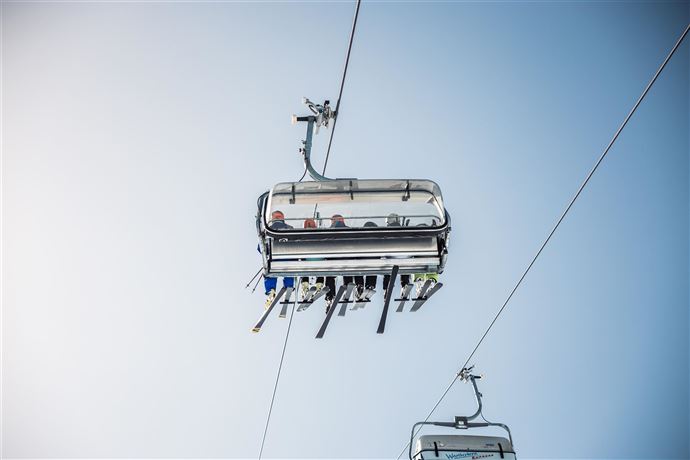 A cable car with passengers floats high in the sky. In the background, a clear blue sky can be seen.