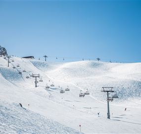 A snow-covered ski resort with several chair lifts. The sky is clear and blue, perfect for a day of skiing.