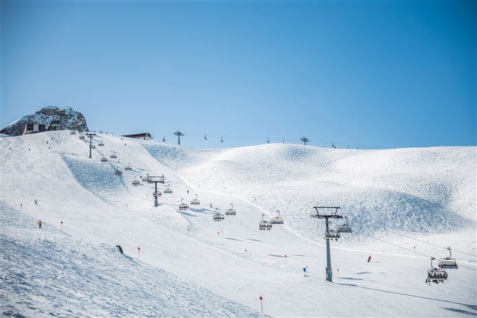 Ein schneebedecktes Skigebiet mit mehreren Sesselliften. Der Himmel ist klar und blau, ideal für einen Skitag.
