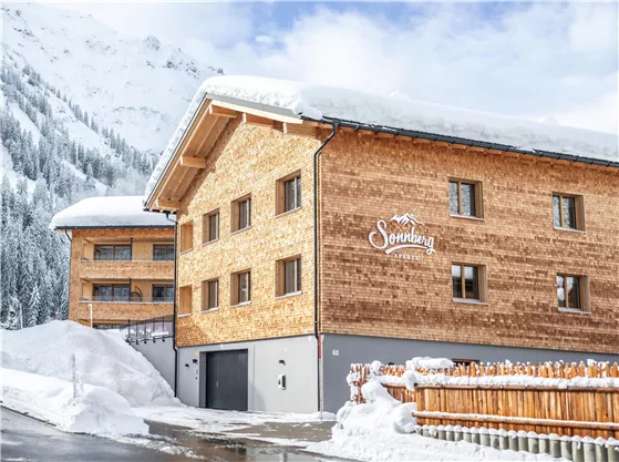 A charming wooden house in the snow with modern architecture. The surroundings are characterized by mountains and fresh, white snow.